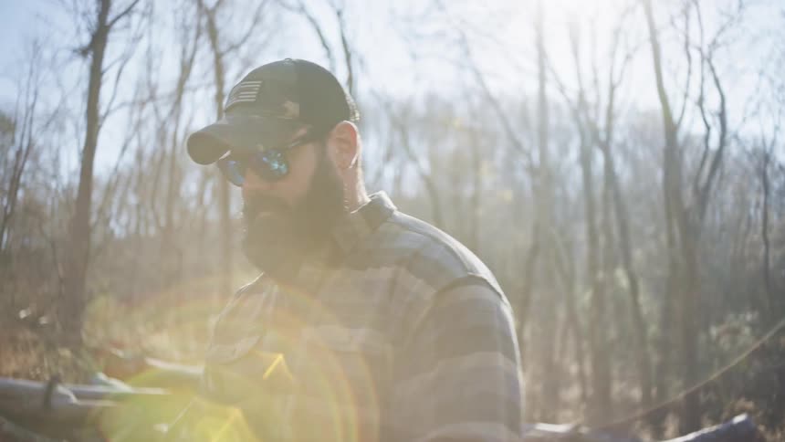 Male tree feller collects and inspects his chainsaw from the back of his truck in a woodland during daytime