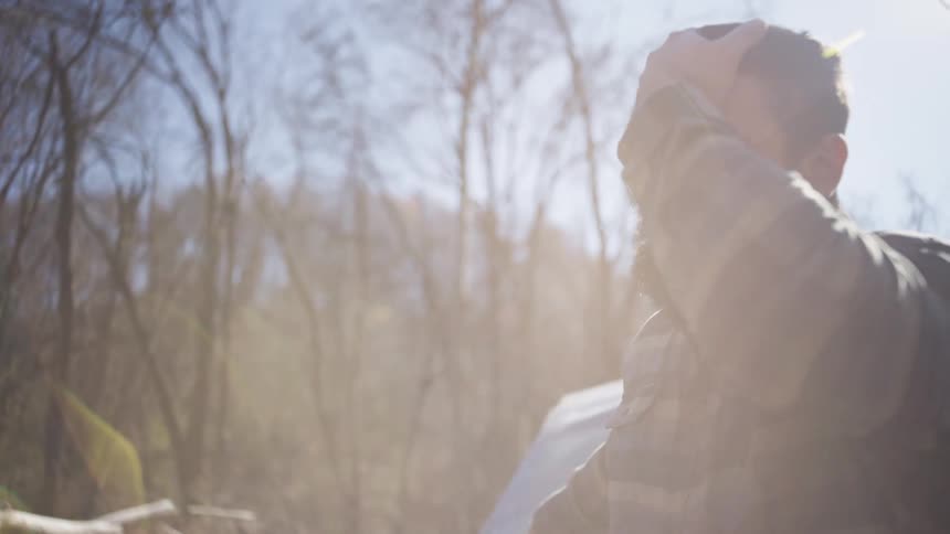 Young male lumberjack leaning against a vehicle removing his gloves and hat outdoors during day time