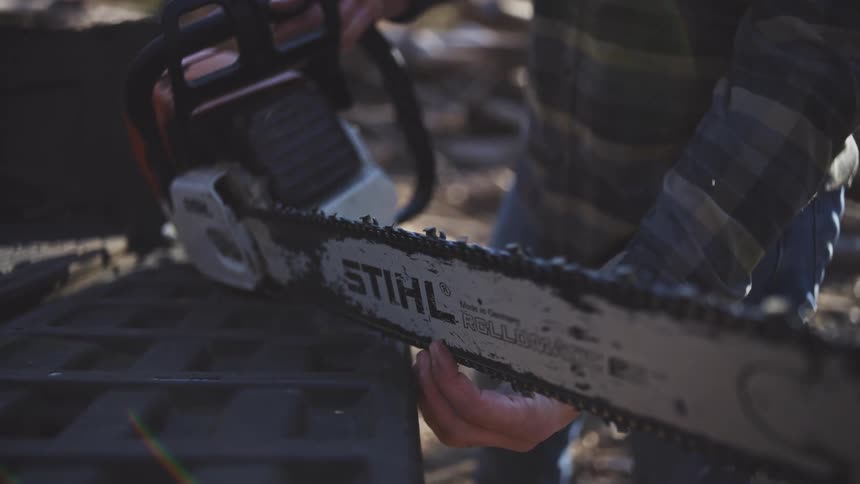 Close up of a male logger handling a chainsaw outdoors in a woodland during daytime