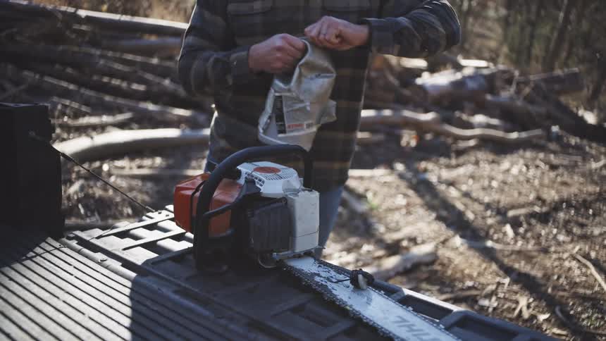 The man puts gasoline in the chainsaw