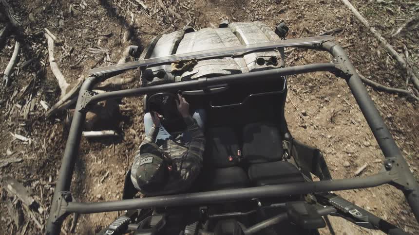 A man driving an open roof vehicle through a woodland during daytime