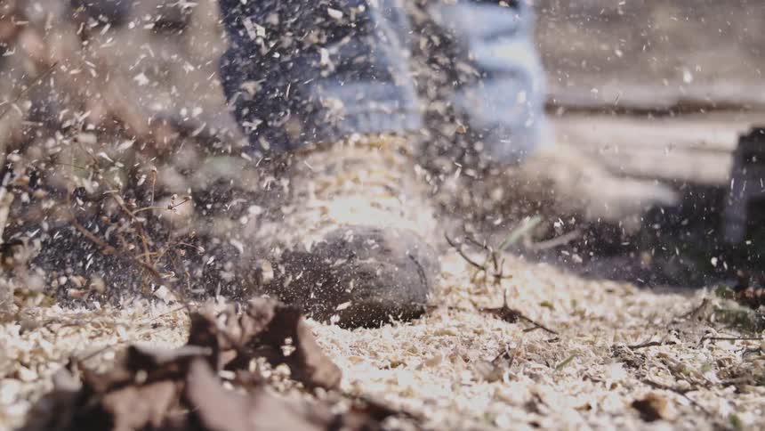 Sawdust falls onto the work boots of a person working outdoors on an autumn day