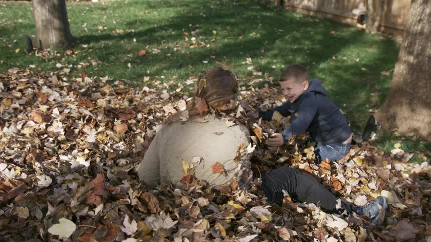 Toddler and a man happily playing with dead leaves on a lawn outdoors during day time