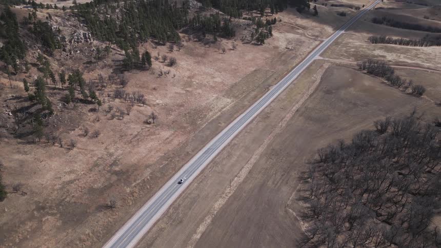 Car drives alone on a road surrounded by dry fields and hills