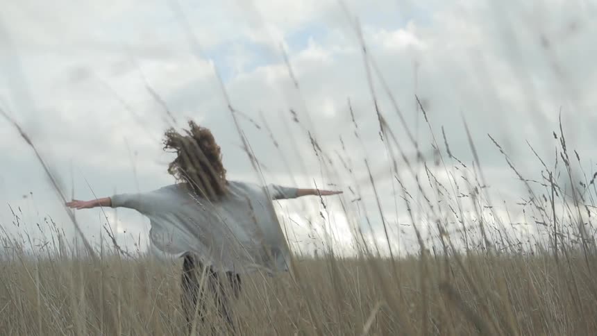 A young woman runs through tall grass with her arms extended