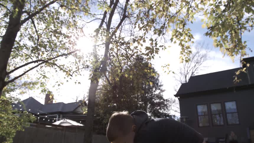Sunlit autumn scene with a boy bent playing in dry leaves in a backyard