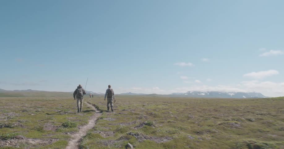 People walking along a trail in an open field under a clear blue sky