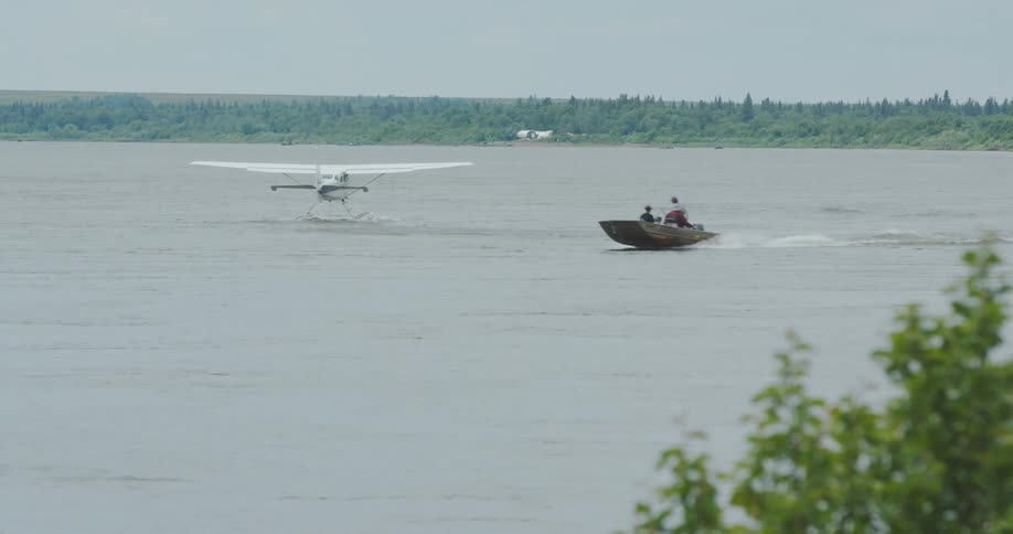 Boat and seaplane moving side by side on a river surrounded by vegetation