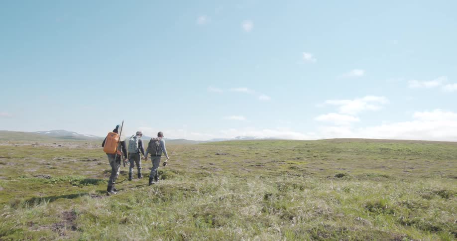 Group of fishermen walking across an open field under a blue sky