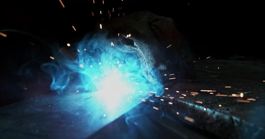Burning light glows blue at the intersection of two man made surfaces as it releases sparks into the dark