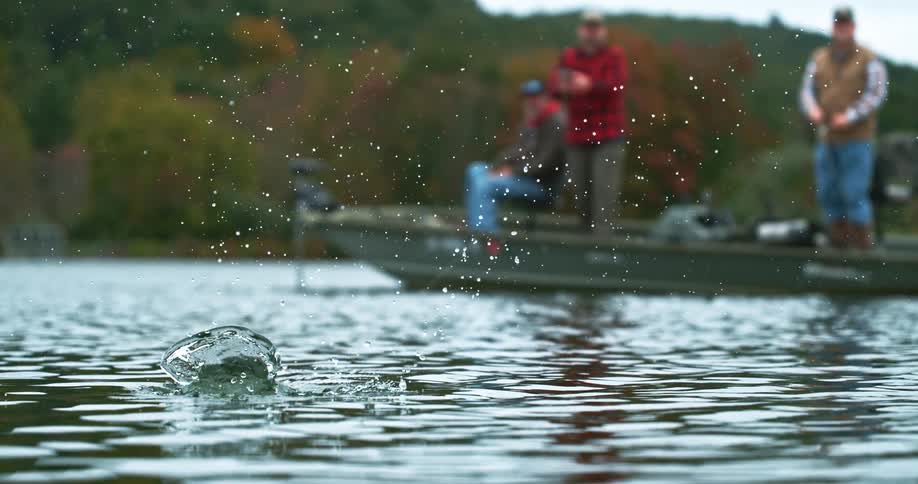 Lures floating on the water with fishermen on a boat in the background surrounded by autumn vegetation