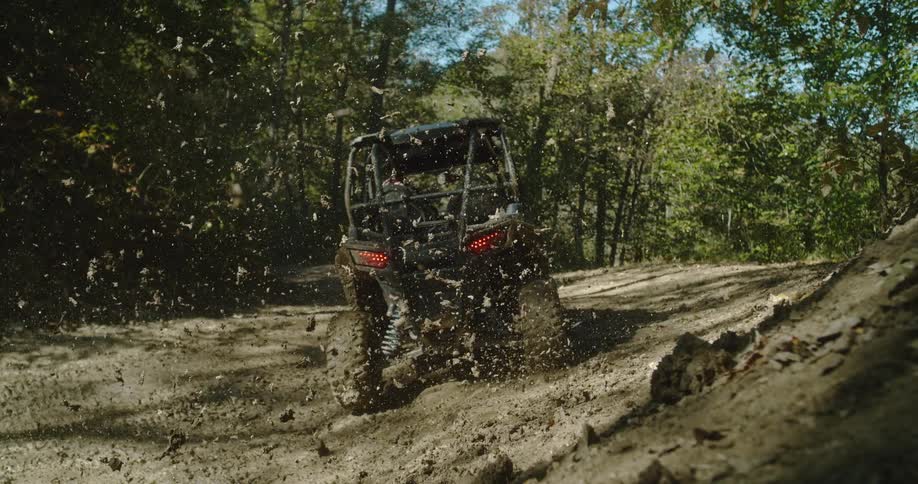 Offroad vehicle kicking up mud while speeding along a trail surrounded by trees