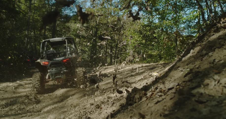 An atv speeds through a puddle in the woods at midday sending muddy water splashing in all directions as it carves through the rugged terrain