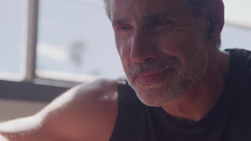 A middleaged man with a grey beard stands exhausted after a workout sweat streaming down his face under the midday sun