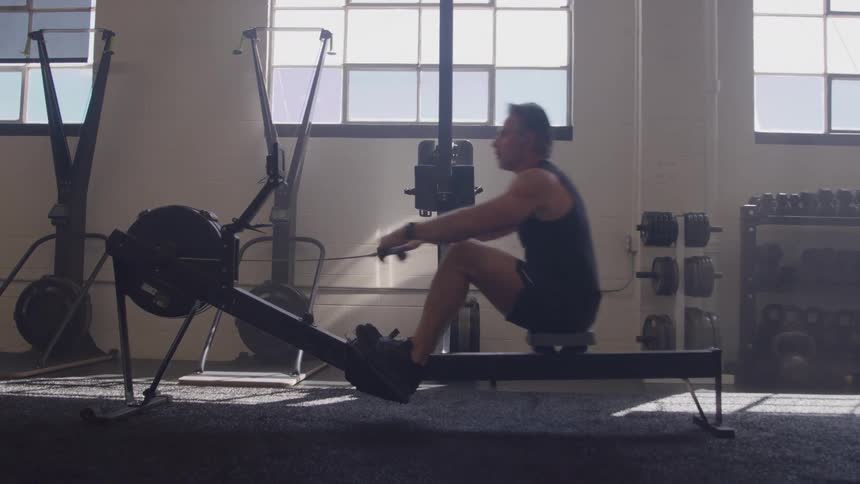 Man training on a rowing machine in a gym lit by natural light