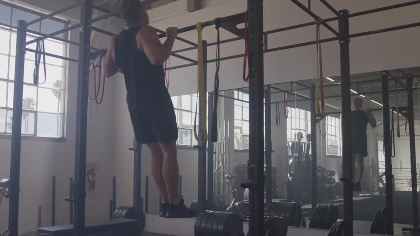 A man performs pullups in the gym wearing a black active shirt and matching shorts his muscles engaged as he lifts himself with focus and strength