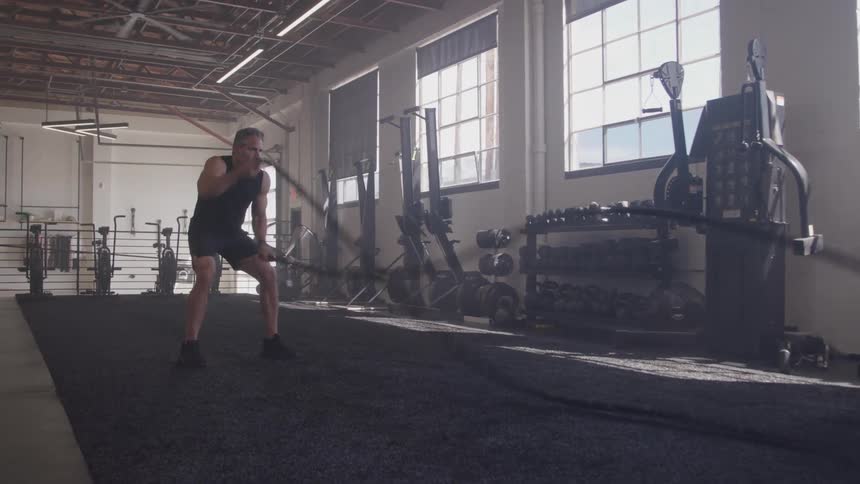 A middle aged man exercising with battle ropes in an indoor gym during daytime