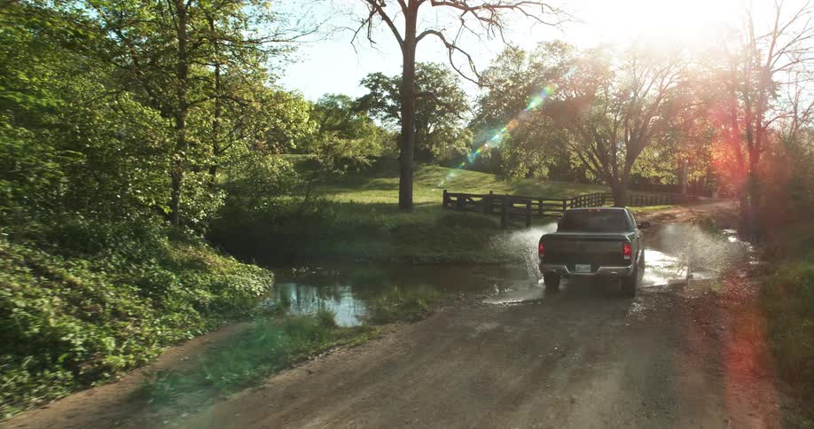 Pickup truck driving through a dirt road with water puddles at sunset