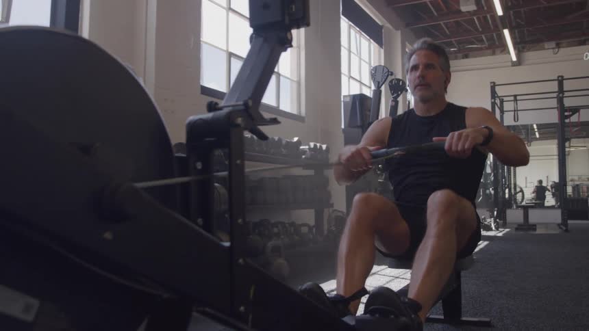 A middle aged man working out with a gym machine in an indoor gym during daytime