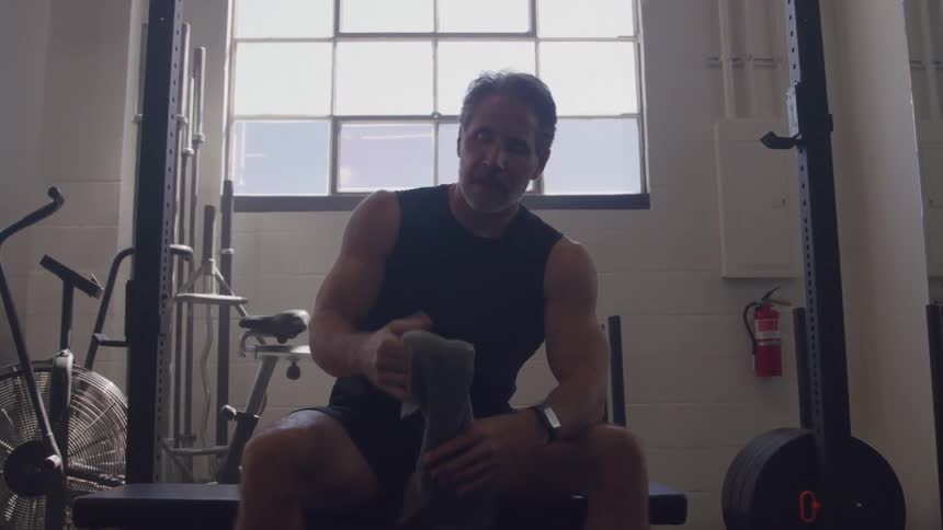 Man sitting on a gym bench wiping his face after a workout