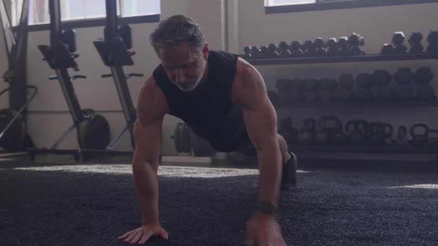 A middleaged man performs pushups in the gym at midday focusing on strength and form as he works through his routine