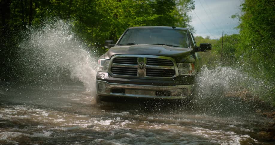 Pickup truck crossing a shallow river section surrounded by vegetation