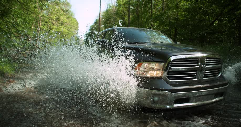 Pickup truck driving through a puddle on a dirt road surrounded by trees