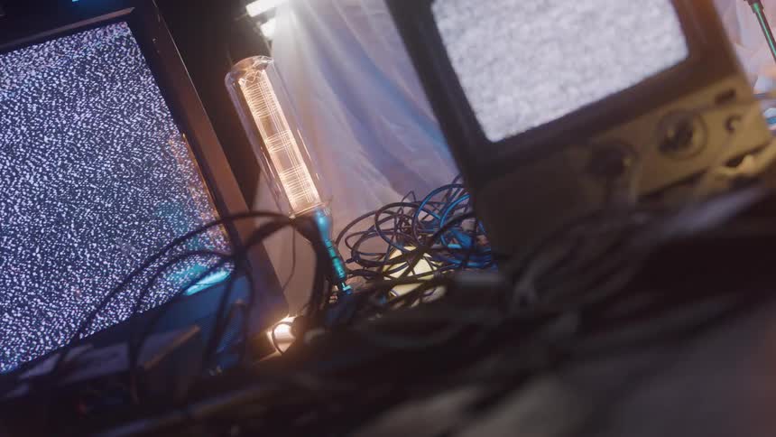 Lowangle view of tangled cables on a floor between two crt monitors showing static lit by a glowing tube light and moody neon