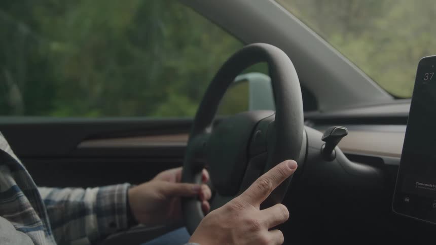 Person driving a car with hands on the steering wheel and a digital dashboard visible