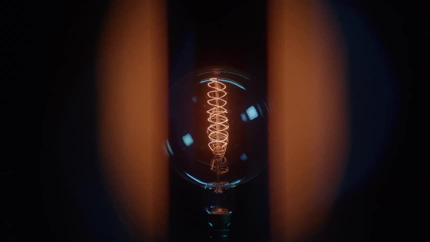 Lit incandescent bulb in focus with a visible spiral filament