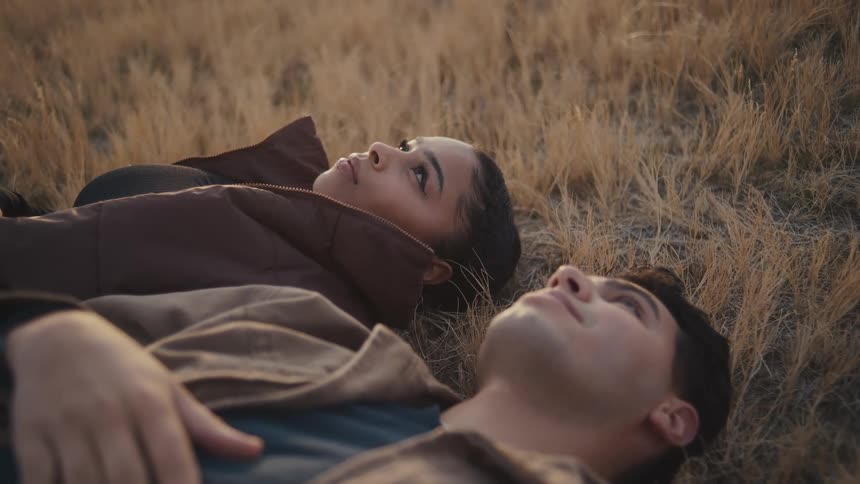 A young couple lay in a field looking up at the sky