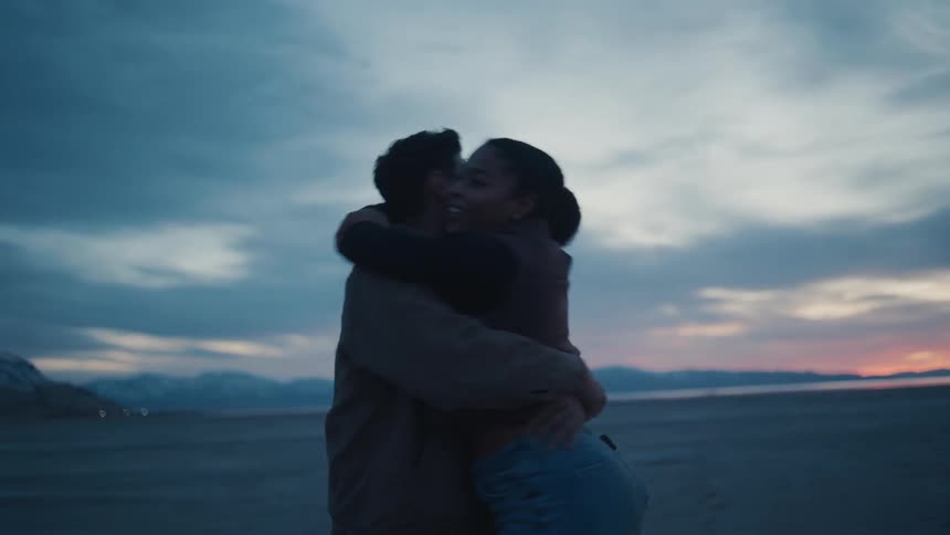 A man and woman hug and spin around on a beach at dusk