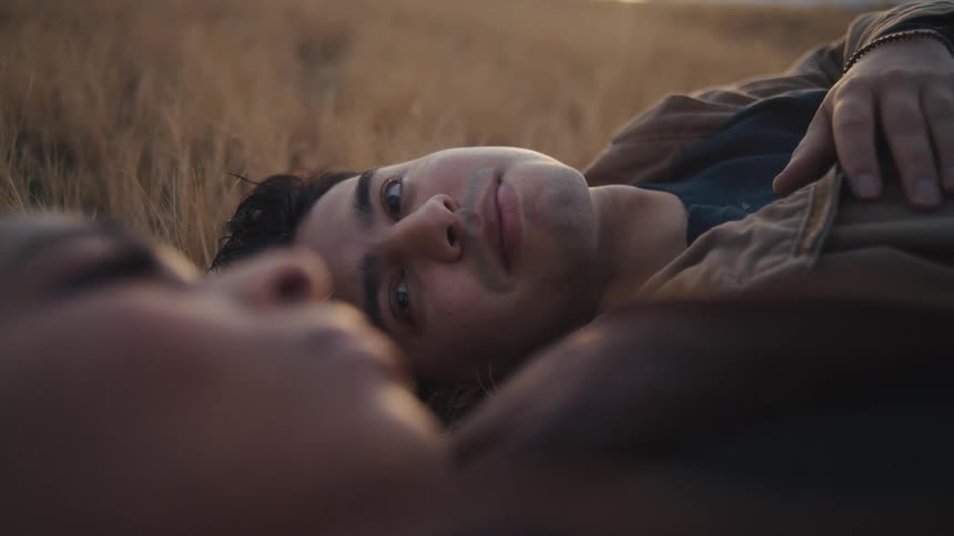 Young man and young woman lying down next to each other on the ground outdoors during dusk or dawn