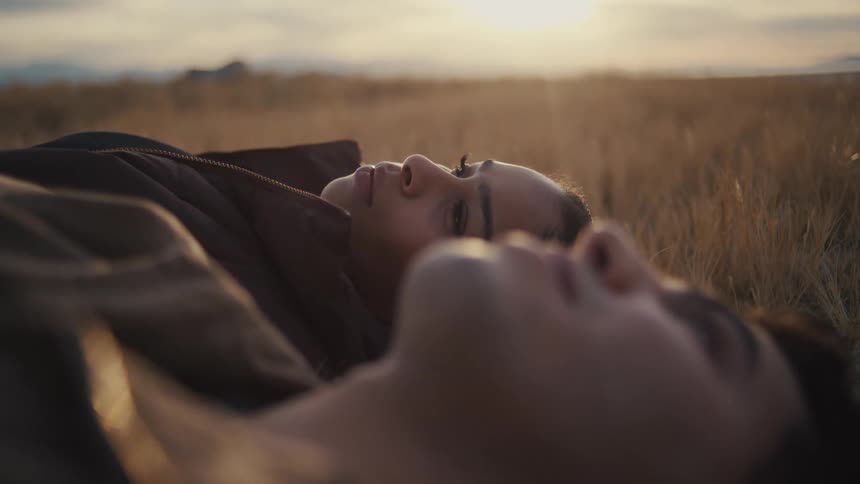 A couple lie in a field at sunset gazing at the sky