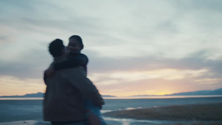 Man picks up a woman and spins aroundon the coast under a red tinted sky