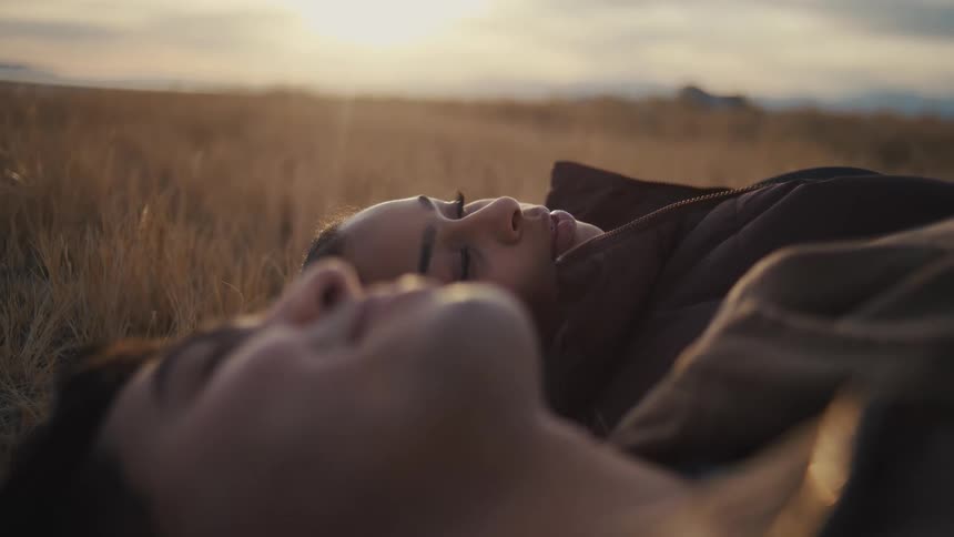Couple smiles while lying in a field and talking on a cloudy autumn day