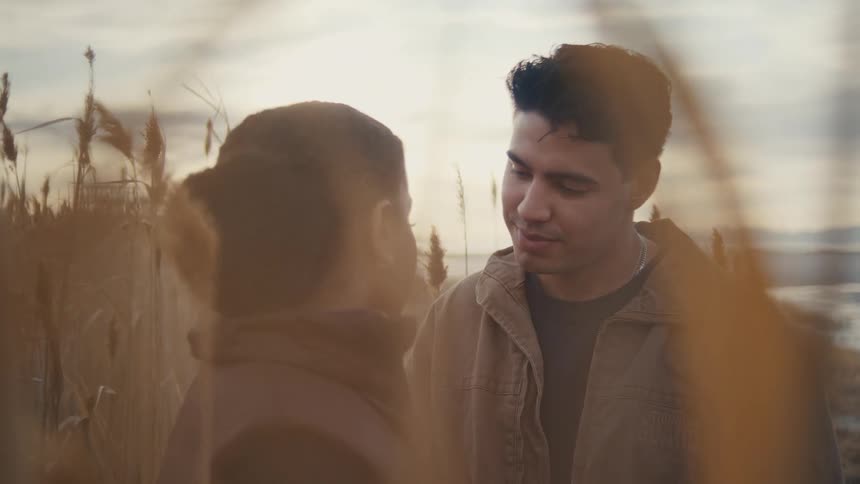 Couple romantically gazes into each others eyes in tall grass at sunset