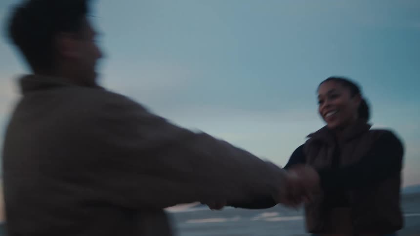 Smiling couple holds hands and spins around while at the coast near dawn