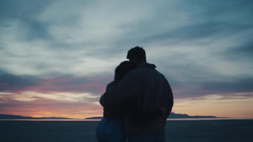 Silhouette of a young man and a young woman kissing and hugging while they watch the sunset or sunrise outdoors
