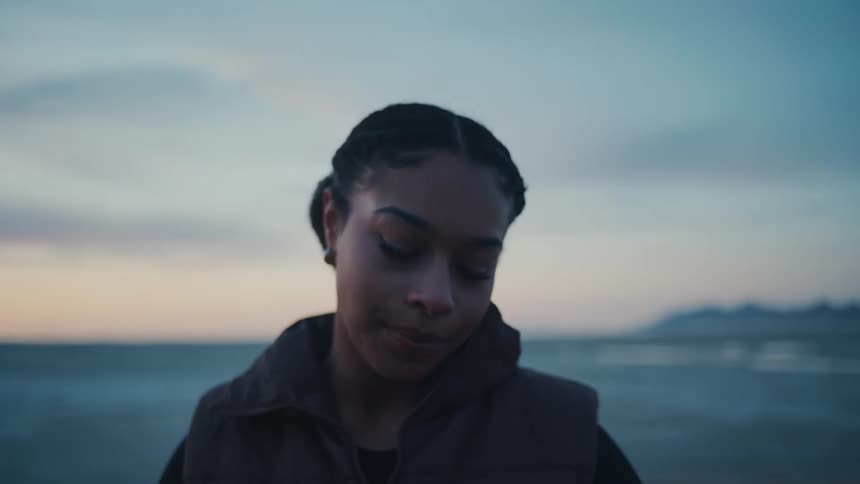 A woman smiles warmly at the camera outdoors at sunset