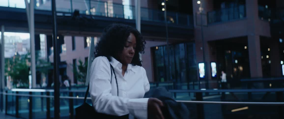 Woman in a white shirt walking through a modern urban area at dusk