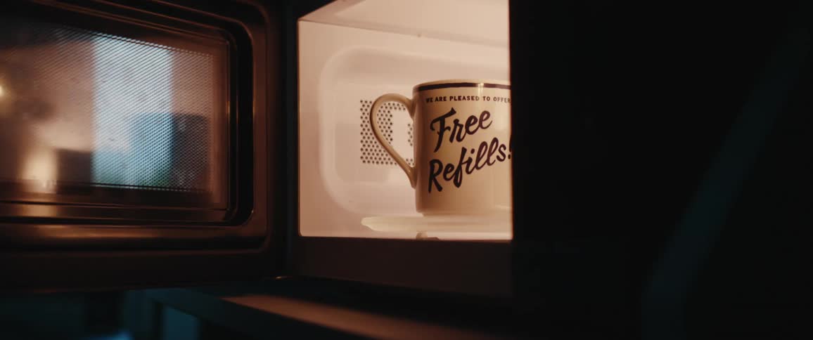 Tattooed hand placing a mug with the phrase free refills inside a lit microwave