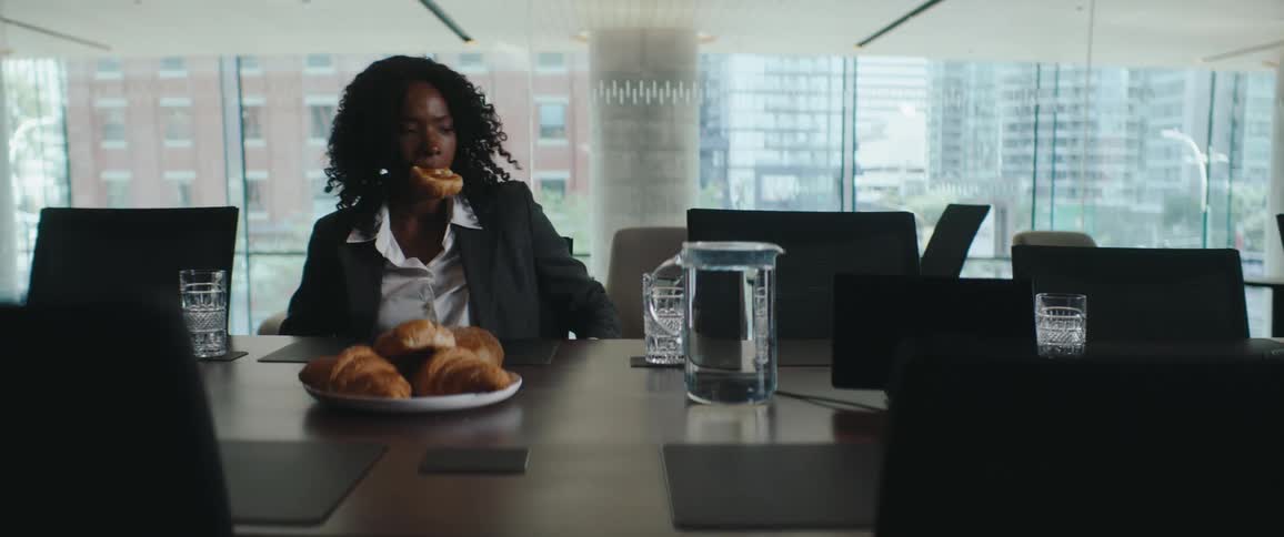 Woman sitting in a meeting room with a croissant in her mouth in front of a set table