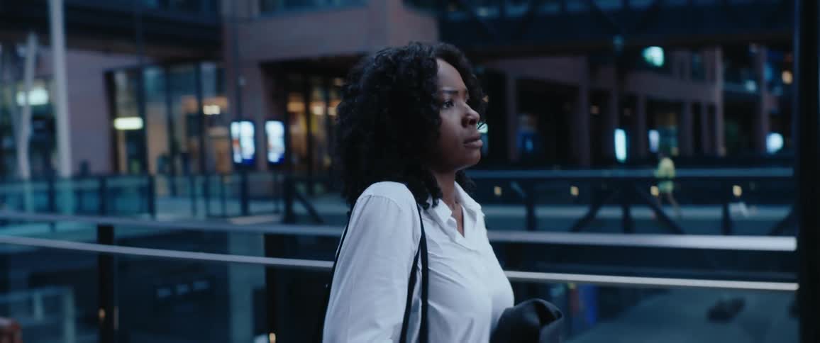 Woman in a white coat walking in an urban area with glass buildings in the background