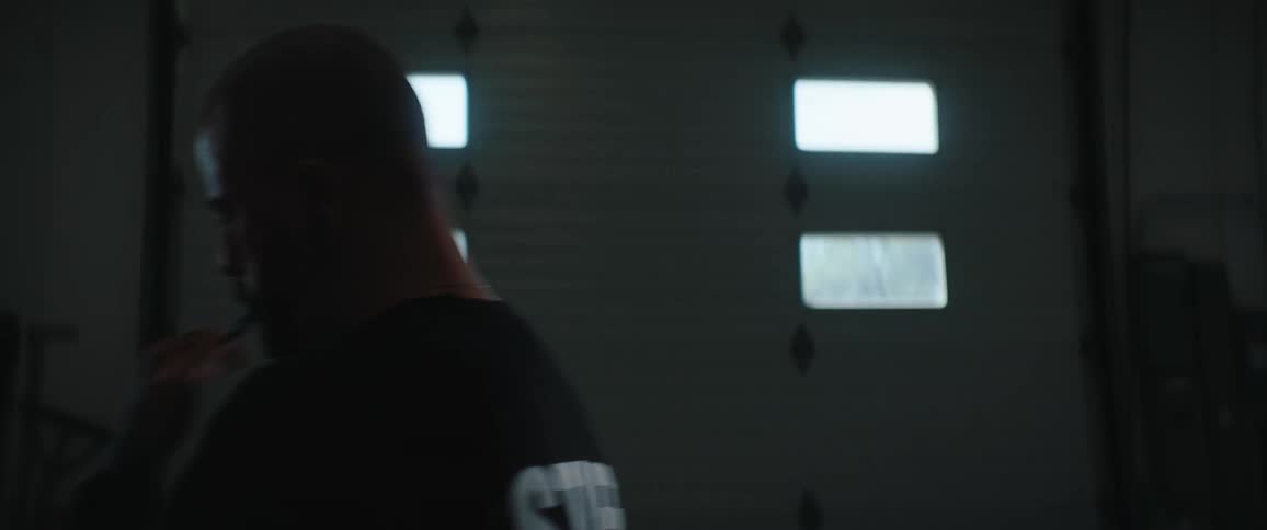 Bald man wearing a black shirt with the word staff written on it walking around indoors while brushing his teeth during day time