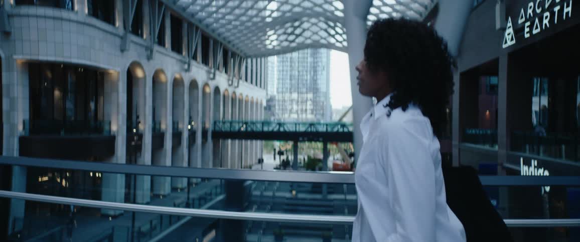 Black woman wearing a white shirt walking fast across a bridge on an urban environment outdoors during day time