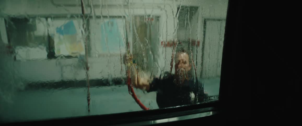 A uniformed worker sprays water on a large window inside a station