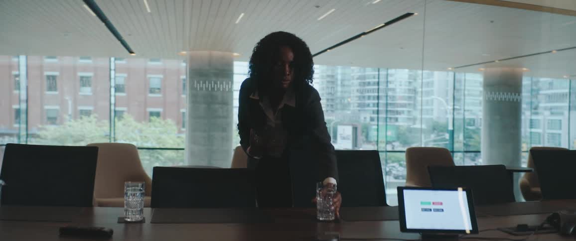 Woman in a suit arranging glass cups on a conference table in a room with large windows