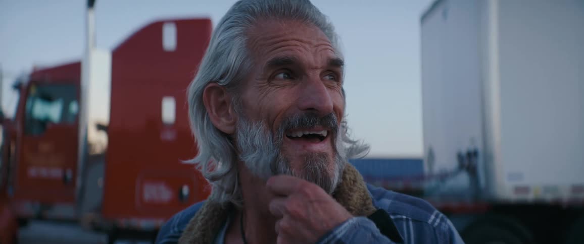 Graybearded man looking to the side in a yard with trucks in the background