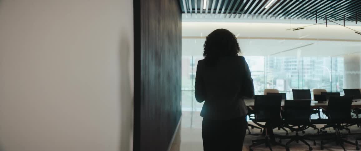 A young woman opens the door and walks into an empty conference room at midday dressed in a suit she carries a set of glasses and carefully spreads them across the table preparing the space with quiet precision